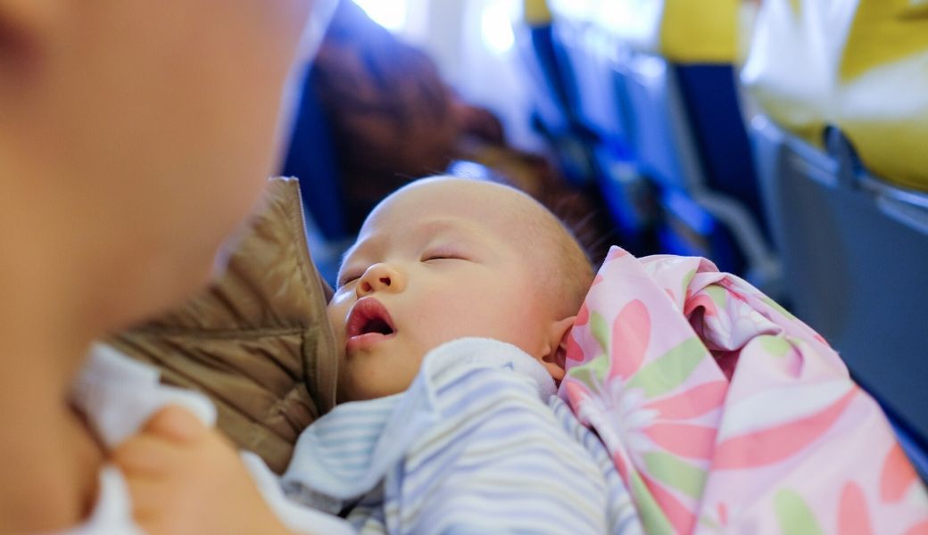 Tips for flying with an infant or baby for this mom holding her sleeping infant on airplane