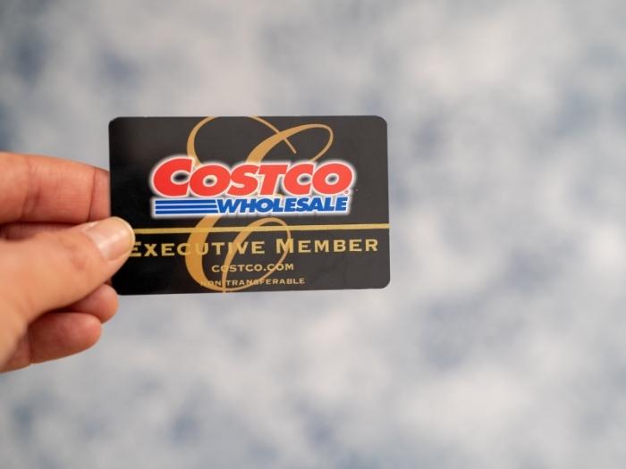 A black Executive Member Costco membership card held by a left hand with gray blurred background