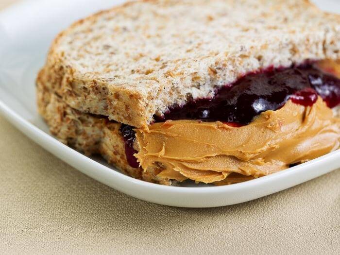 Closeup horizontal photo of a peanut butter and jelly sandwich cut in half, inside white plate on textured beige table.