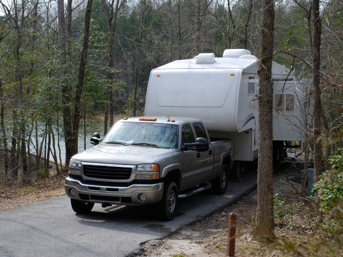 A fifth wheel parked on a roadside woods with a lake view