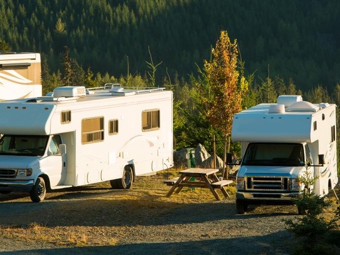 2 class b motorhome parked in a camp ground with a picnic table