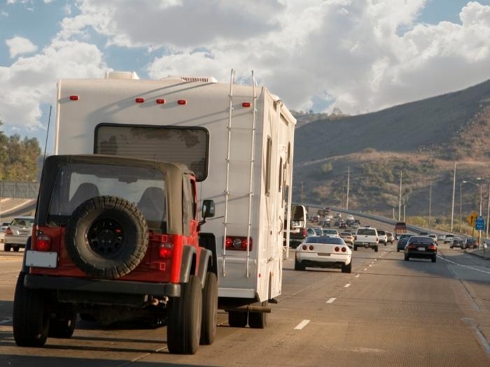 An RV pulling a red black jeep in a highway