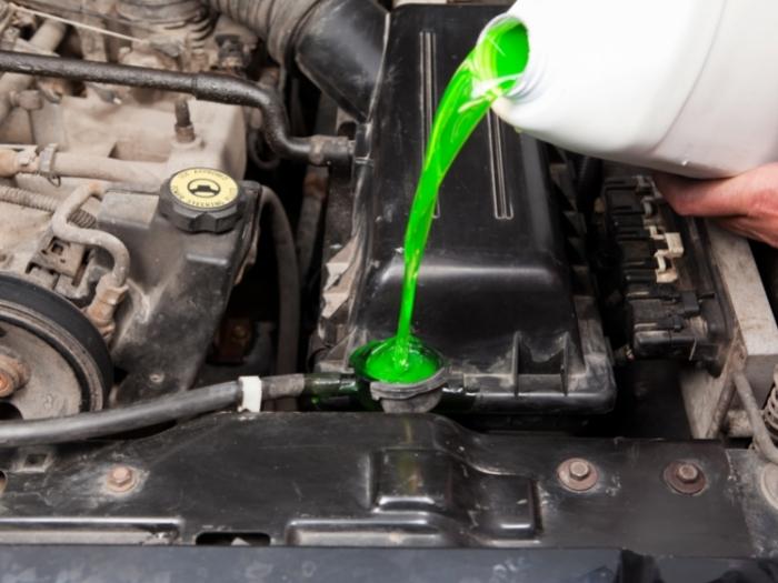 A close shot of a mechanic's hand pouring antifreeze into a vehicle's radiator.