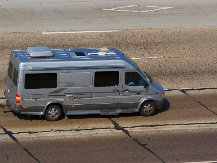 A gray class B van-like with gray and black accent swoosh stickers RV being driven by the middle of the road. road.