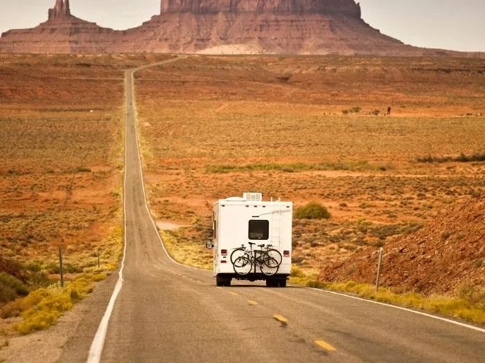 A rear shot of an RV driving on a long deserted highway with mountain views in front
