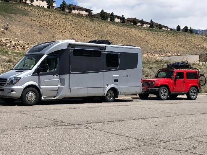 A class b motor home towing a red jeep