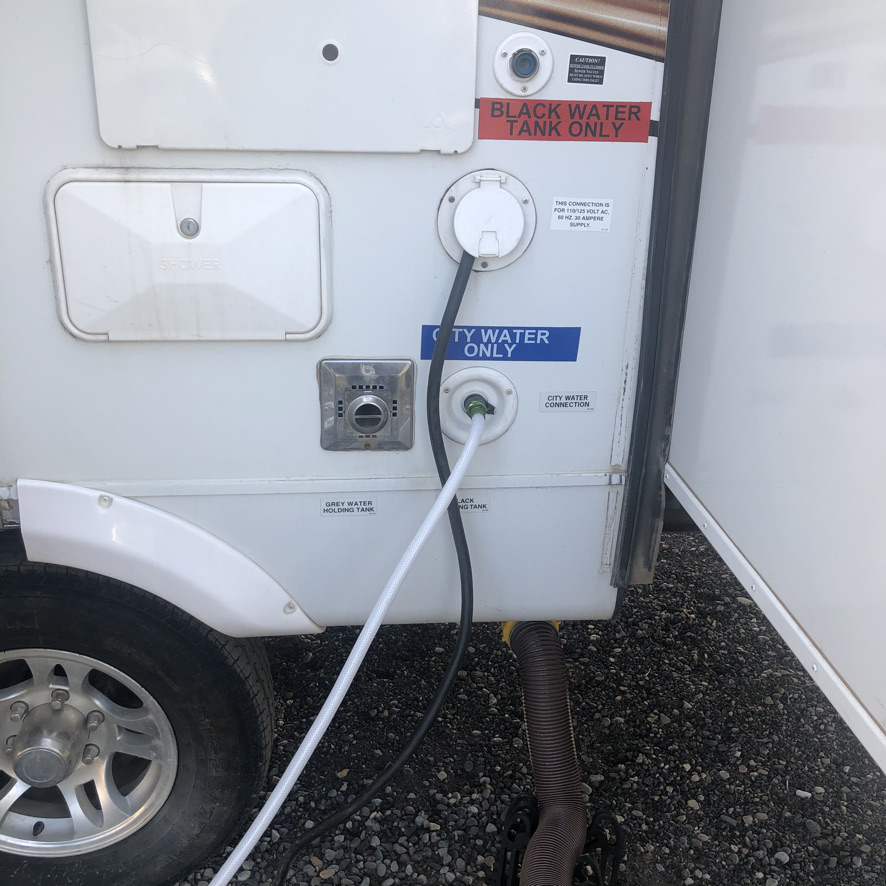 Side of RV showing various hookup spots for water, electric and sewer