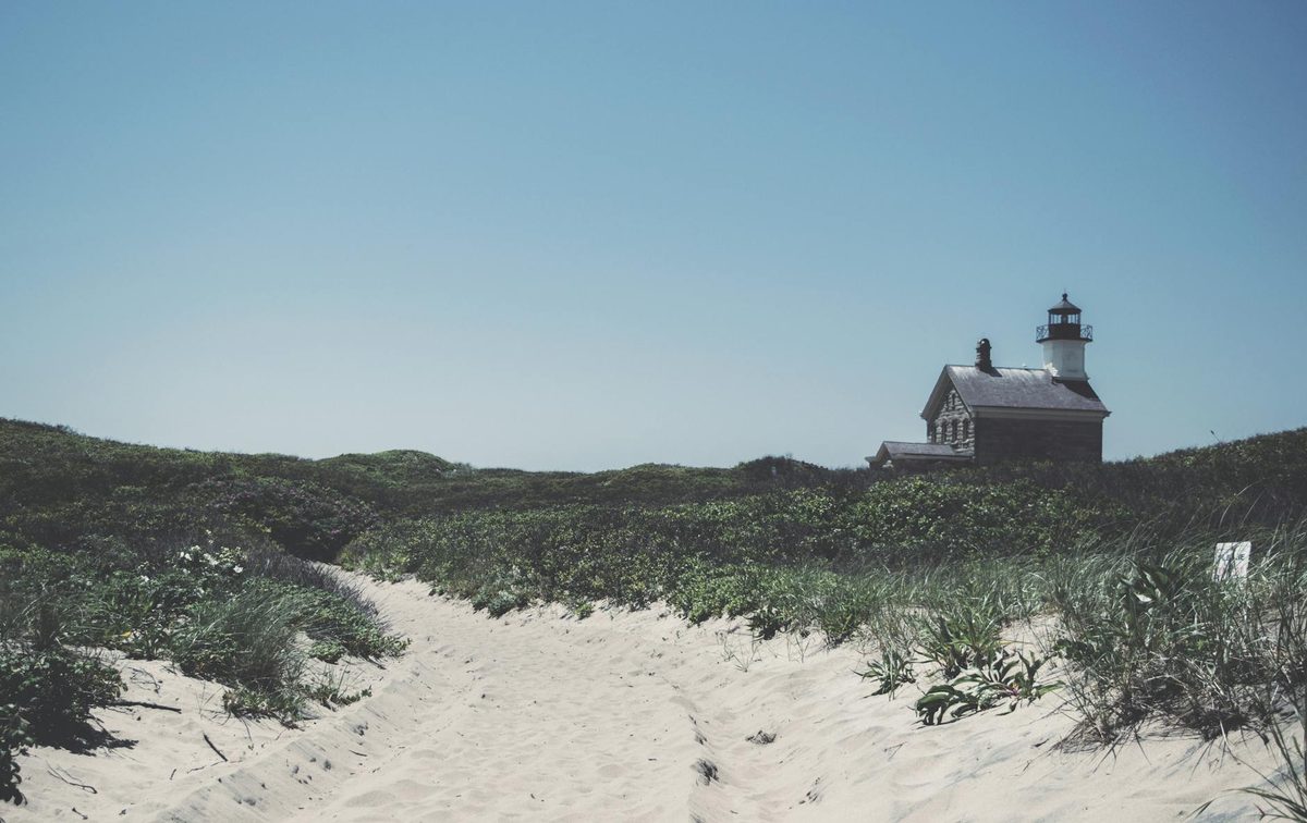 Block Island lighthouse with sandy path leading through grassy dunes under a clear blue sky