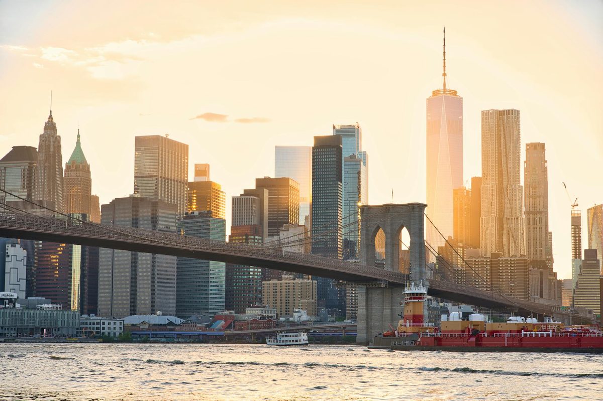 Brooklyn Bridge and the New York City skyline at sunset with warm golden light reflecting off the water