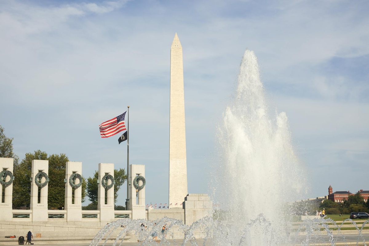 The Washington Monument with American flags and a fountain under a bright blue sky
