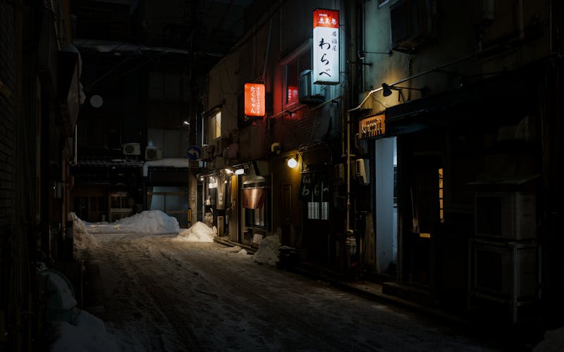 Snow-covered alley in Kanazawa at night with restaurant lights