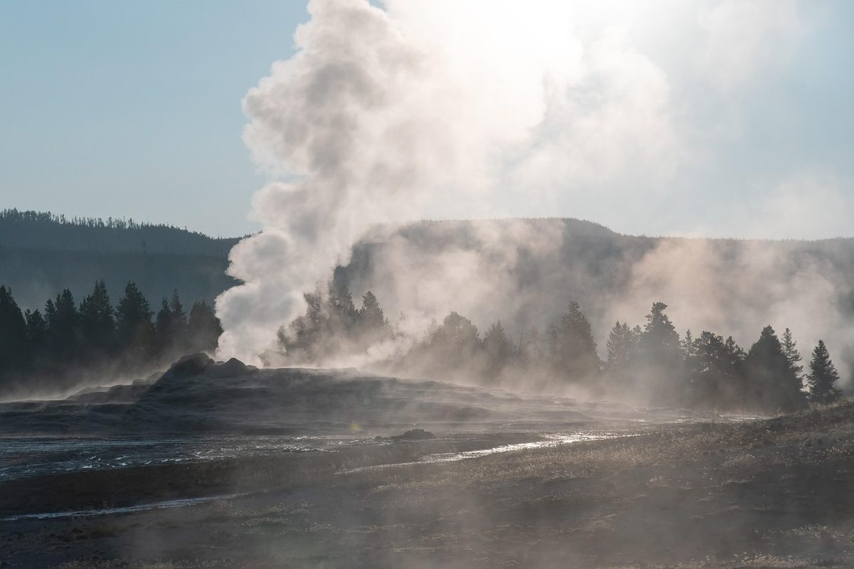 Yellowstone geyser erupting with steam against blue sky