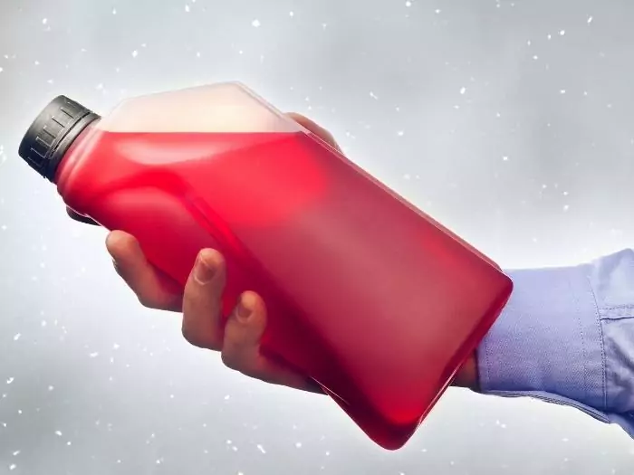 Male hand holding a bottle of antifreeze additive water-based liquid for winter condition driving.